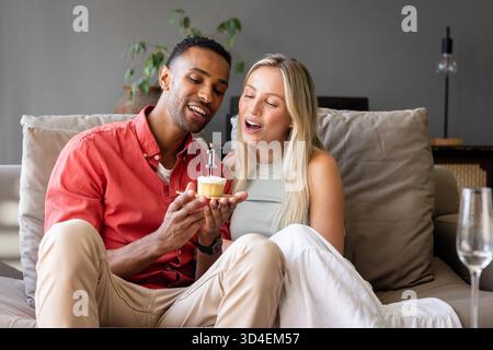 Festeggiare con il cupcake, coppia sorridente sul divano, condividere momenti speciali insieme. Celebrazione, felicità, relazione, insieme, gioia, amicizia || modello rilasciato Foto Stock