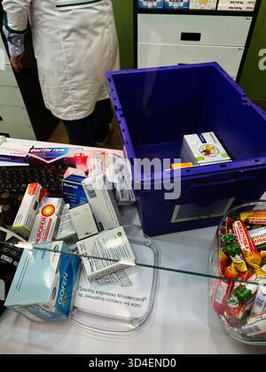 Kiev, Ucraina - 10 novembre 2025: Farmacista in un bancone con medicinali, scatole e una cassa blu in un negozio clinico. Foto Stock