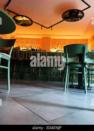 Kiev, Ucraina - 10 novembre 2025: Un elegante ambiente bar con posti a sedere verdi, bottiglie sugli scaffali e illuminazione calda. Foto Stock