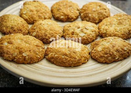 10 biscotti ANZAC appena sfornati su un piatto di bambù, appena usciti dal forno. Foto Stock