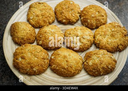 10 biscotti ANZAC appena sfornati su un piatto di bambù, appena usciti dal forno. Foto Stock