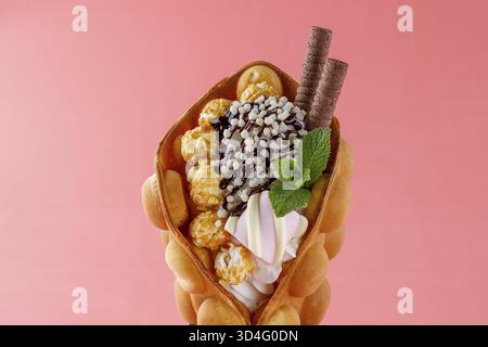 Cibo, Un cono dorato per waffle con bolle d'uovo ripieno di panna morbida, salsa al cioccolato sgusciata, perle croccanti spolverate, grappoli di popcorn al caramello, ciao Foto Stock