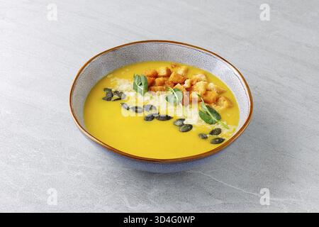 Cibo, zuppa liscia di purea di zucca servita in una ciotola rustica in ceramica con crostini croccanti semi di zucca tostati parmigiano e microgreen freschi Foto Stock