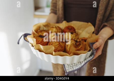 Mani femminili che tengono una teglia rotonda con mele cotte al forno Foto Stock