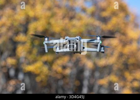 Un moderno drone sospeso in aria davanti ad alberi decorati con colori autunnali, pronto per i video e i servizi fotografici. Il concetto di natura e tecnica Foto Stock