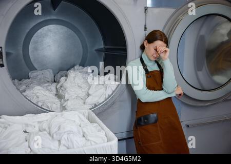Lavoratrice stanca si trova di fronte a una lavatrice che le copre gli occhi Foto Stock