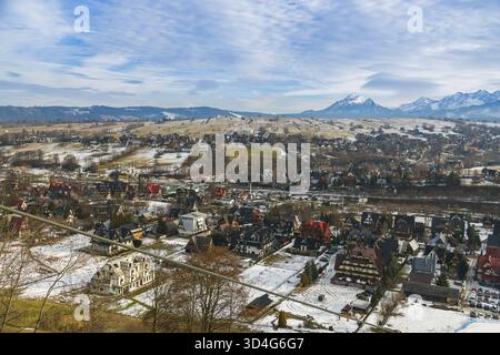 Una vista di Zakopane, Polonia, rivela edifici in stile alpino sparsi in una valle. Le cime innevate del Tatra si innalzano sullo sfondo, addossate a un clou Foto Stock