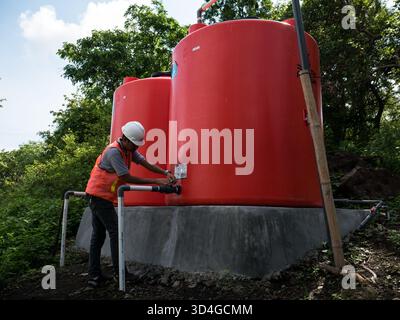 Sidenreng Rappang, Indonesia - 20 dicembre 2019: Operaio in un elmetto che controlla la valvola di grandi serbatoi d'acqua rossi. Foto Stock