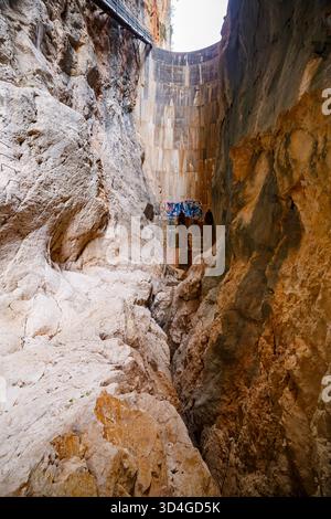 Una vista dal fondo di una profonda gola rocciosa, che mette in risalto l'impressionante altezza della curva di cemento della diga di Isbert sopra, con aspre maree erosive Foto Stock