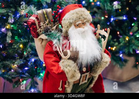 Una bambola di Babbo Natale si erge circondata da colorate luci natalizie e presenta una gioiosa scena di vacanza piena di allegria. Foto Stock