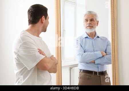 Giovane uomo che si vede come anziano nello specchio. Concetto di personalità, passato e futuro, flusso del tempo, età Foto Stock