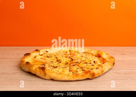 Pizza al formaggio appena sfornata su un tavolo di legno con sfondo arancione, luce calda e croccante consistenza della crosta Foto Stock