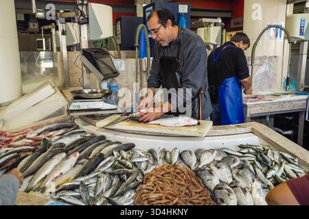 Lagos, Portogallo, 8 novembre 2025, un pescivendolo pulisce un pesce dietro una mostra di pesce appena pescato al mercato locale. Foto Stock