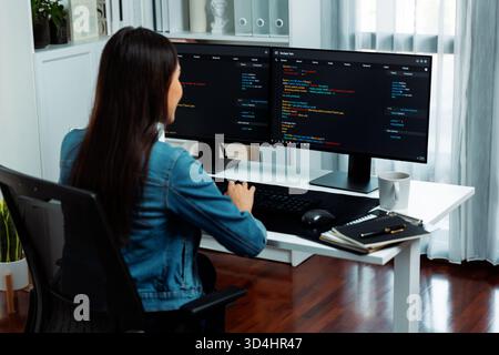 Giovane asiatico sviluppatore IT che crea con la digitazione di informazioni online sul pc con i dati del programma di codifica dell'applicazione del sito web, indossando maglietta jeans Foto Stock