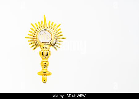 Dettaglio di un mostro dorato con il simbolo religioso IHS su sfondo bianco. Immagine minimalista che rappresenta la fede, la spiritualità e il cattolico Foto Stock