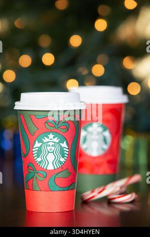 Dallas, Texas - 9 novembre 2025: Starbucks Coffee nei nuovi 2025 bicchieri natalizi. Esposto con bastoncini di caramelle su un tavolo di legno. Bokeh natalizio Foto Stock