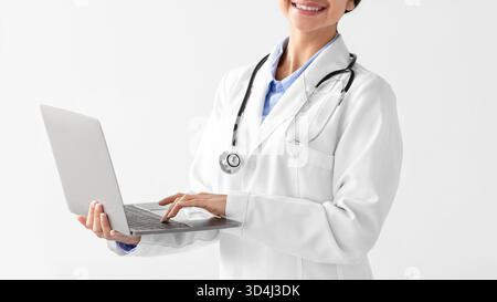 Il giovane dottore indiano in cappotto bianco fornisce consulenze a distanza utilizzando la tecnologia moderna Foto Stock