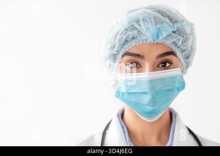 Ritratto di una giovane dottoressa indiana in equipaggiamento protettivo che guarda direttamente la fotocamera Foto Stock
