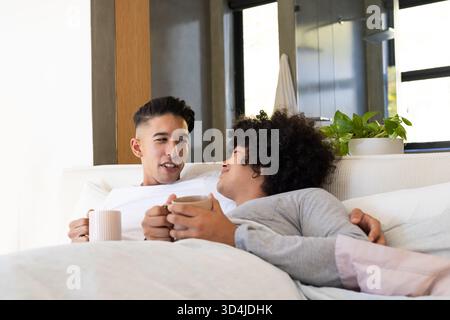 Coccolatevi con diverse coppie di uomini che si trovano insieme sul letto in una camera da letto moderna, con tazze da caffè in ceramica Foto Stock