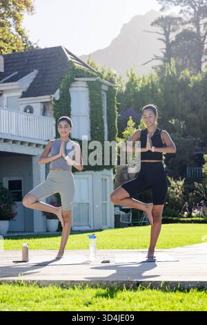 Pratica yoga diverse amiche che tengono in posa gli alberi sul ponte del cortile, con tappetini da yoga Foto Stock