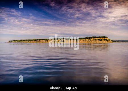 Un suggestivo paesaggio telefotografico di un'isola boscosa o di una scogliera costiera sullo stretto di Puget, che mostra le scogliere e gli alberi dettagliati, con acque calme nel mare Foto Stock