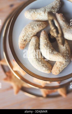 Primo piano del tradizionale Vanillekipferl appena sfornato, spolverato generosamente con zucchero a velo di vaniglia, disposto su un'elegante porzione bianca a due livelli Foto Stock