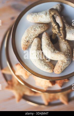 Primo piano del tradizionale Vanillekipferl appena sfornato, spolverato generosamente con zucchero a velo di vaniglia, disposto su un'elegante porzione bianca a due livelli Foto Stock