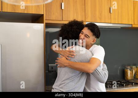 Abbracciate padre e figlio nella moderna cucina, con frigorifero in acciaio inossidabile Foto Stock