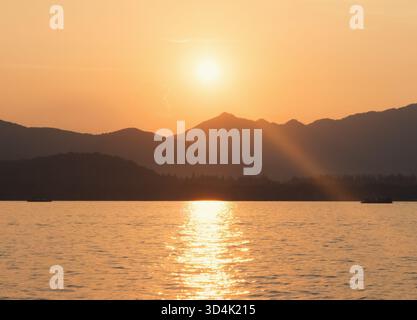 Paesaggio panoramico del Lago Ovest, Hangzhou, durante l'ora d'oro con i raggi del sole che splendono attraverso le montagne lontane Foto Stock