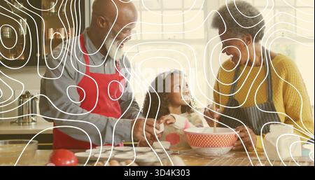 Mescola la coppia di anziani e la nipote nella cucina di casa, indossa grembiuli e usa un recipiente rosso Foto Stock