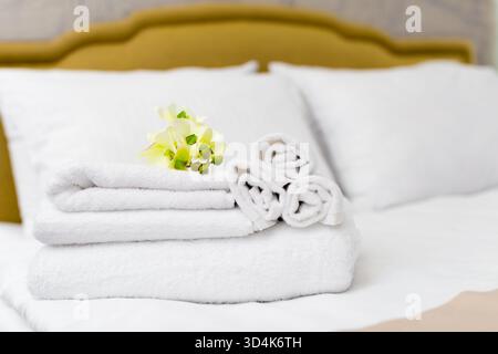 Morbidi asciugamani bianchi disposti in modo ordinato su un letto con fiori in un ambiente accogliente Foto Stock