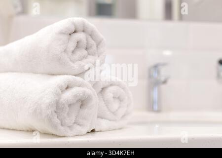 Asciugamani bianchi morbidi e soffici impilati in modo ordinato in un luminoso ambiente da bagno Foto Stock