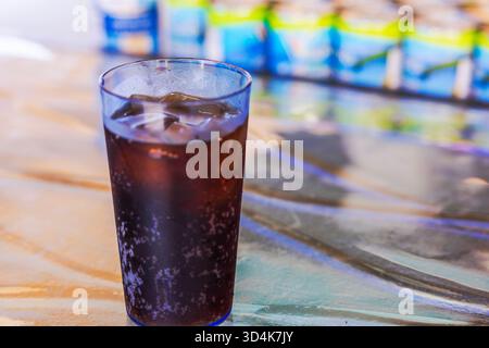 Vista ravvicinata di un bicchiere con bibita fredda e cubetti di ghiaccio sullo sfondo di bottiglie colorate sfocate. Aruba. Foto Stock