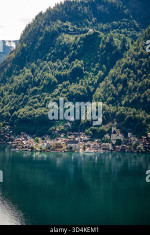 Vista aerea degli edifici di Hallstatt accoccolati su una lussureggiante e verdeggiante montagna, riflessa nelle tranquille acque di Hallstatter SEE, Hallstatt, Upper A. Foto Stock