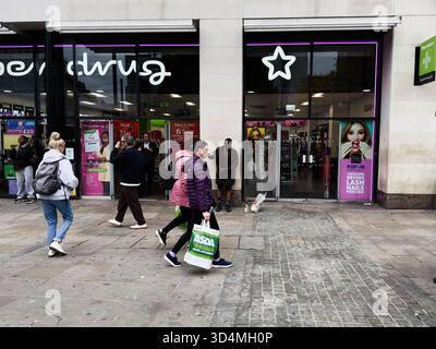 Manchester, Regno Unito - 30 settembre 2025: Gli amanti dello shopping passano davanti ai negozi di Manchester Street, trasportando borse e dirigendosi verso i negozi di Superdrug. Foto Stock