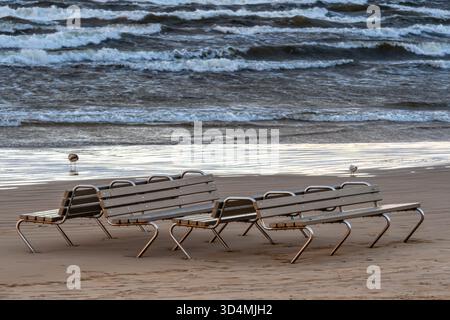 Panchine sulla riva al tramonto con dolci onde che si infrangono sulla sabbia Foto Stock