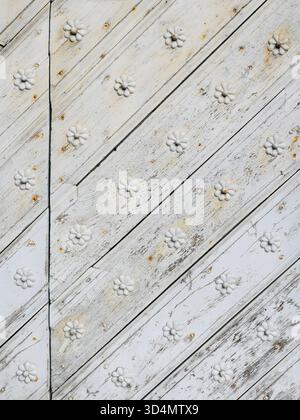 Porta in legno bianco intemprato con tavole diagonali, macchie di ruggine e rosette decorative. Copyspace Foto Stock