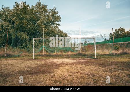 Vecchio obiettivo da calcio su campo irregolare e usurato con erba danneggiata e terreno polveroso, simbolo del tempo e dell'uso. Messa a fuoco selettiva. Foto Stock