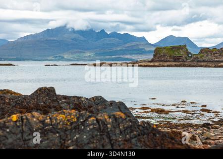 Costa rocciosa con alghe marine e piscine di marea che si affacciano sulle rovine del castello di Dunscaith e sulle montagne Cuillin sull'isola di Skye, Scozia, riflettono il loro splendore Foto Stock