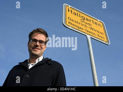 Oestrich Winkel, Germania. 11 novembre 2025. All'ingresso della città, il sindaco Carsten Sinß (SPD) si trova di fronte a un nuovo cartello con la scritta "Hallgarten Stadt Oestrich-Winkel - Rheingau-Taunus-Kreis". Alla fine di ottobre, tutti e dieci i cartelli della città di Oestrich-Winkel nel distretto di Rheingau-Taunus furono rubati. Credito: Michael Brandt/dpa/Alamy Live News Foto Stock