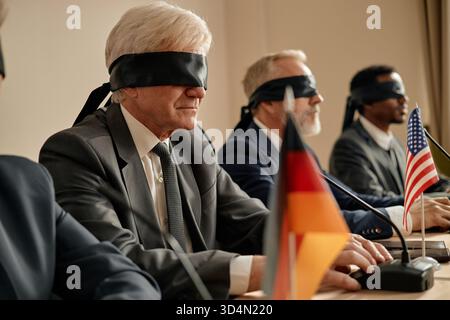 Uomini caucasici anziani e uomo nero seduti bendati al tavolo da conferenza Foto Stock