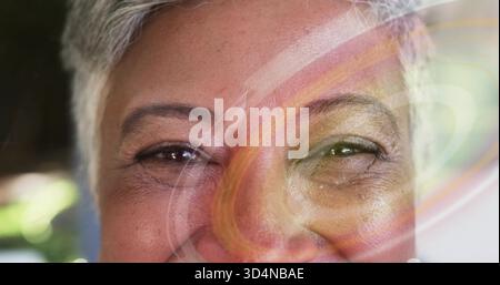 Mostra una donna matura con i capelli grigi sorridente in una stanza interna con turbolenza colorata e bokeh Foto Stock