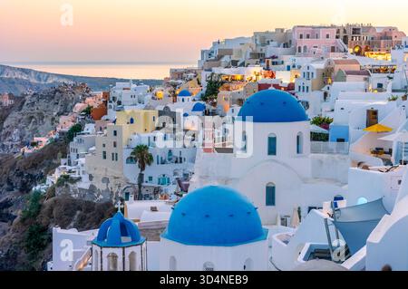 Oia Santorini al tramonto. Le persone ammirano le iconiche chiese a cupola blu e le vedute della caldera Foto Stock