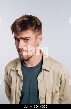 Un giovane uomo è in piedi con un leggero sorriso, vestito con una camicia e una t-shirt casual. Ha i capelli corti e una barba leggera, creando un'atmosfera rilassata Foto Stock