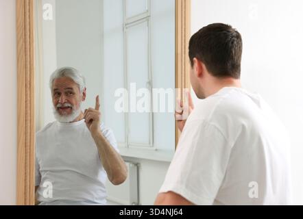 Giovane uomo che si vede come anziano nello specchio. Concetto di personalità, passato e futuro, flusso del tempo, età Foto Stock