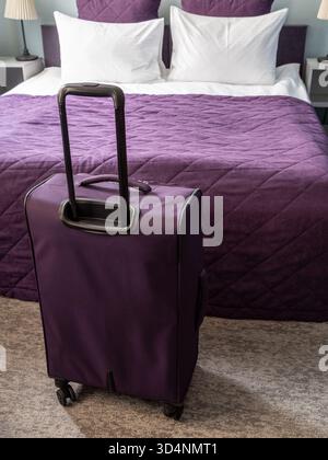 valigia da viaggio viola e letto matrimoniale con biancheria bianca e viola in un piccolo soggiorno Foto Stock