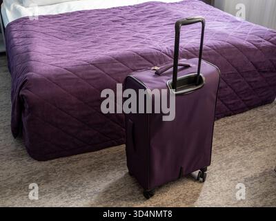 valigia da viaggio viola e copriletto viola su un letto matrimoniale nel piccolo soggiorno Foto Stock