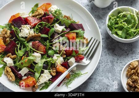 Cibo, primo piano di arancia fresca e sana, barbabietola, insalata di feta e noci su piatto bianco, vista dall'alto Foto Stock