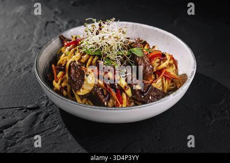Cibo, manzo salato fritto in padella con verdure e spaghetti guarniti con germogli, servito in un'elegante ciotola Foto Stock