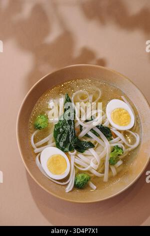 Cibo, Una calda e confortevole ciotola di zuppa di noodle udon con uova tagliate a metà e verdure fresche Foto Stock